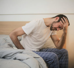 exhausted man sitting at the side of a bed