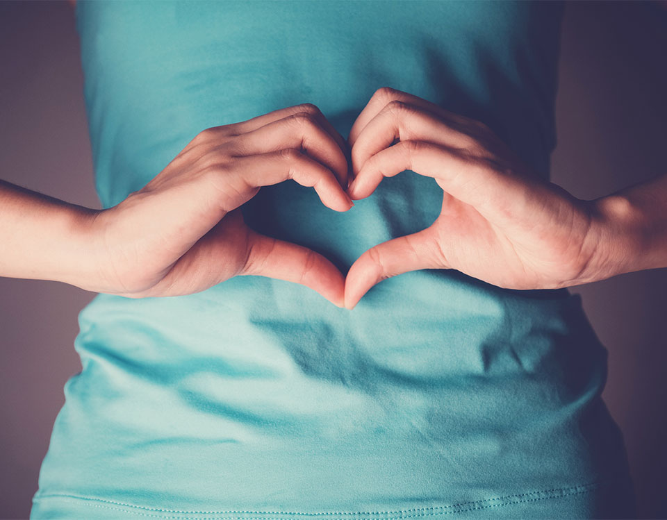 person with hands in the shape of a heart over gut