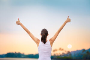 Young woman with arms in the air giving thumbs up.