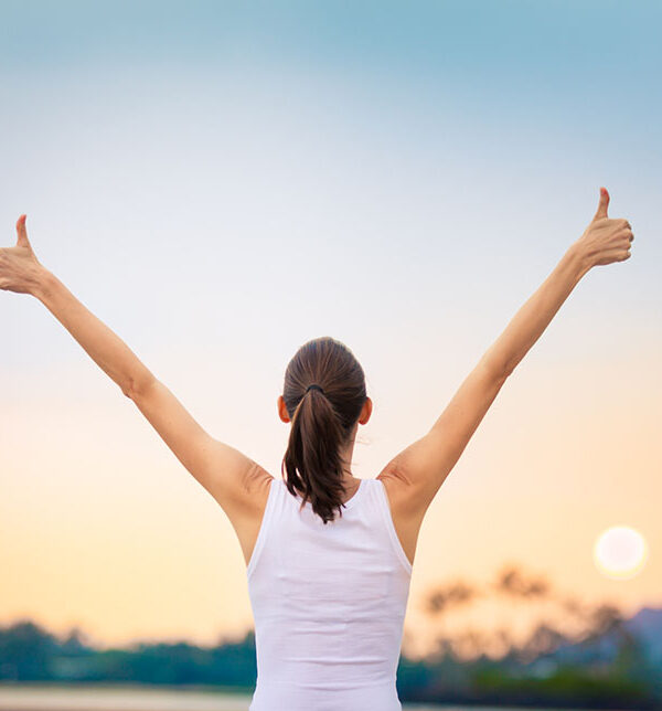 Young woman with arms in the air giving thumbs up.