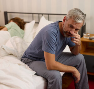 Mature man looking worried while his wife sleeps in the background